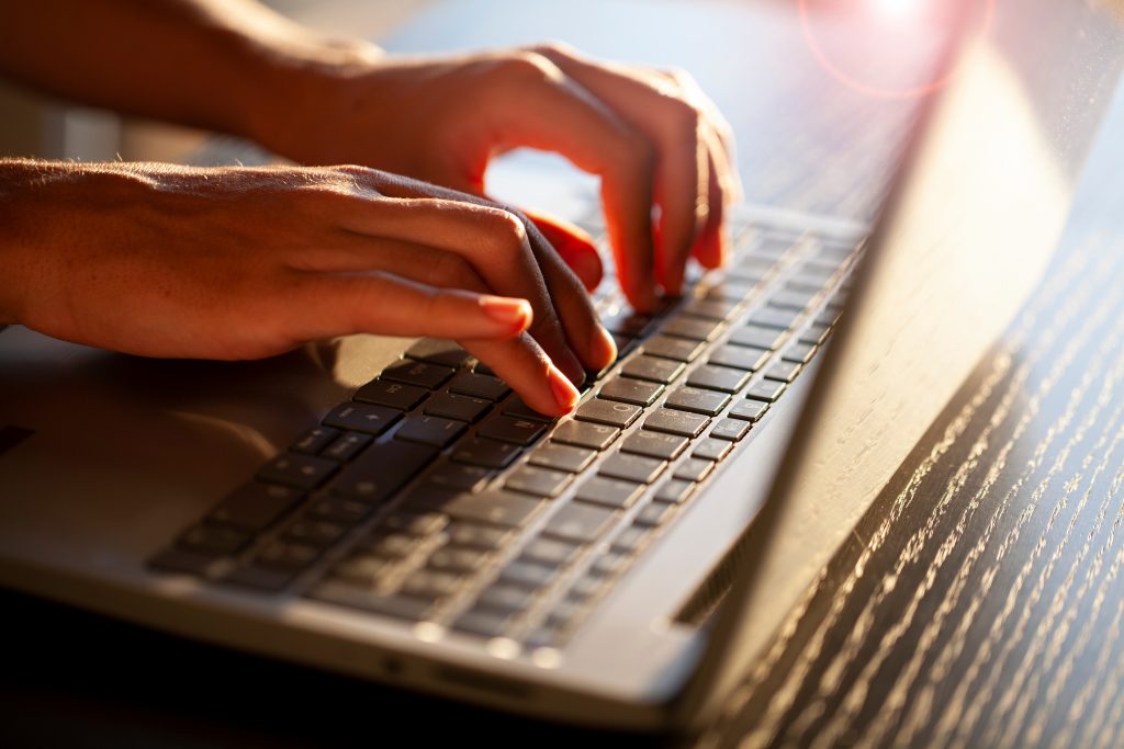 Manos escribiendo en ordenador portátil. Imagen vía Adobe stock