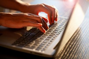 Manos escribiendo en ordenador portátil. Imagen vía Adobe stock